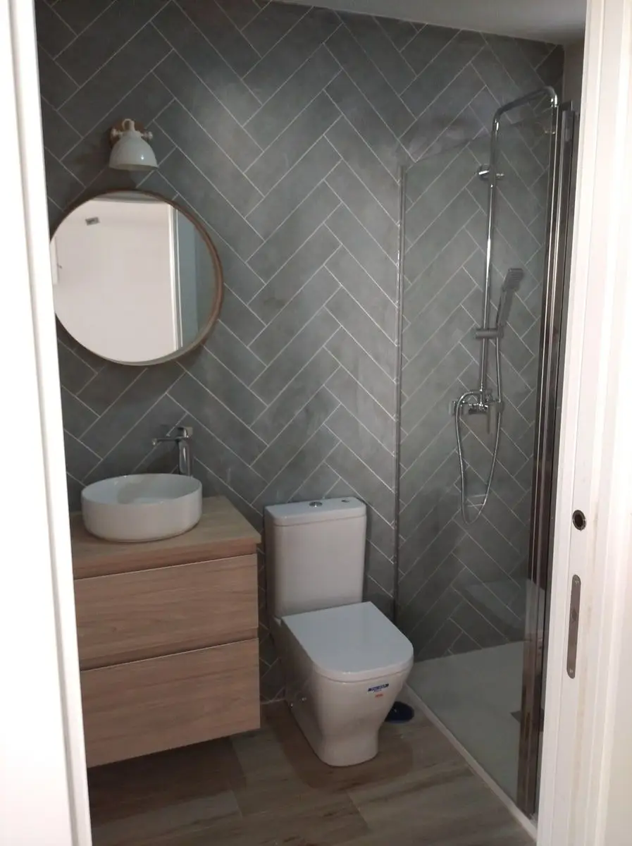 Baño reformado con alicatado en espiga, lavabo sobre encimera y ducha