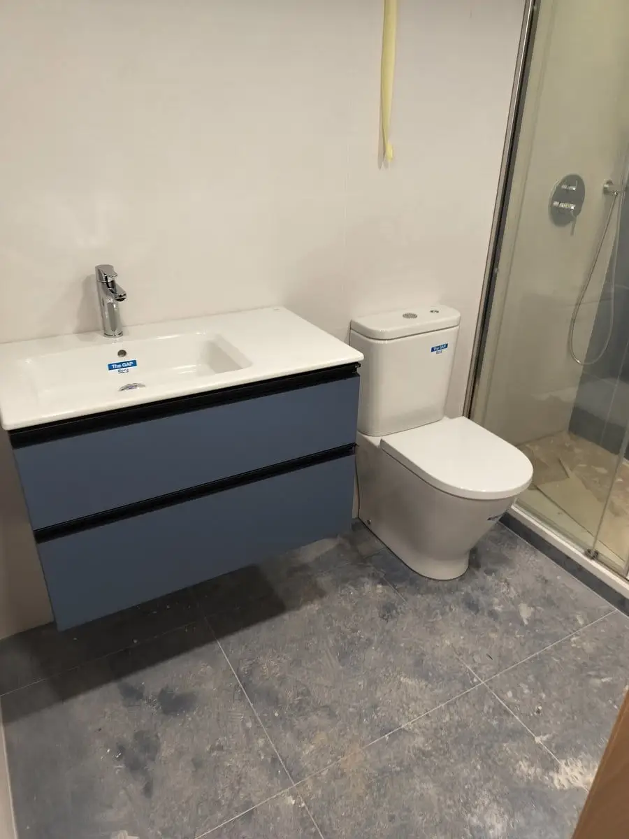 Baño con mueble suspendido azul, inodoro y mampara de ducha